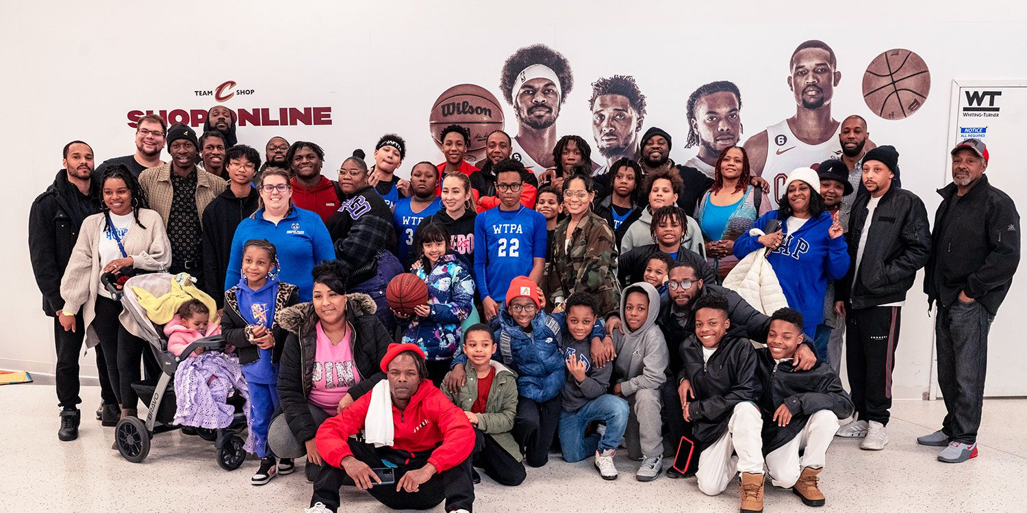 Large group of adults and children posing in front of basketball player graphics.