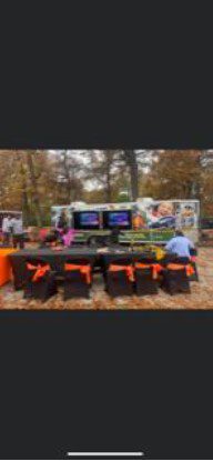 Outdoor event with truck, screens, tables, and chairs.