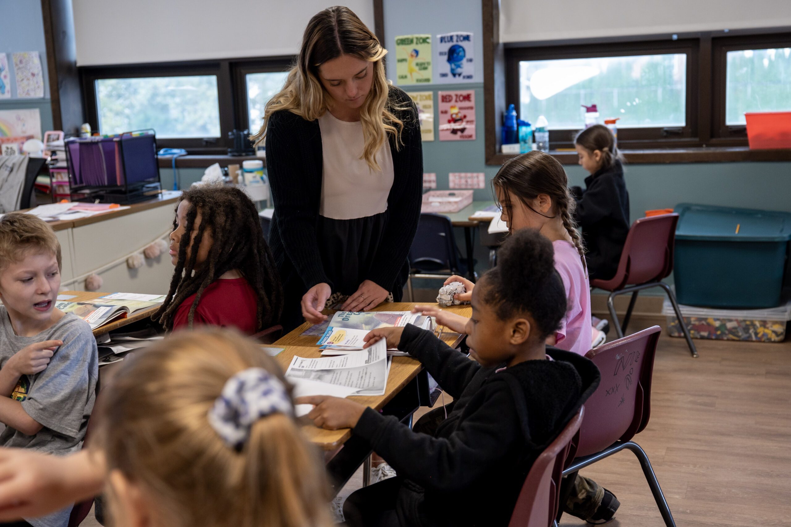 Adult and children interacting at desks in a classroom.