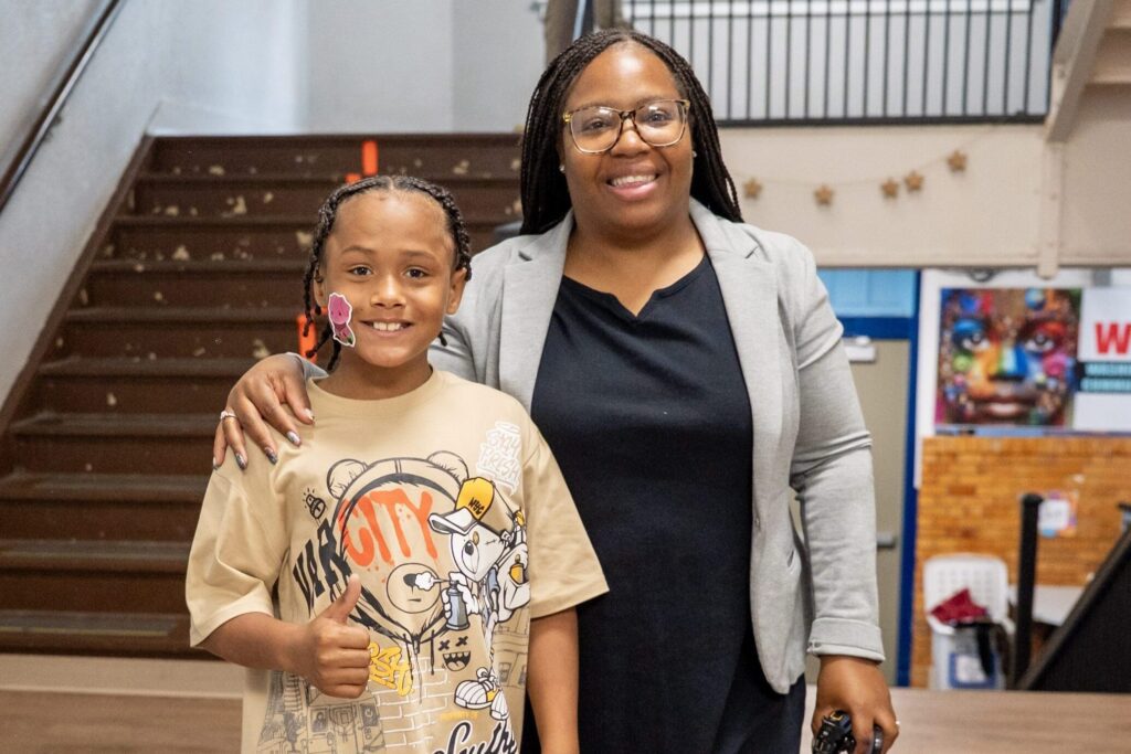 Adult and child smiling, child gives thumbs up.