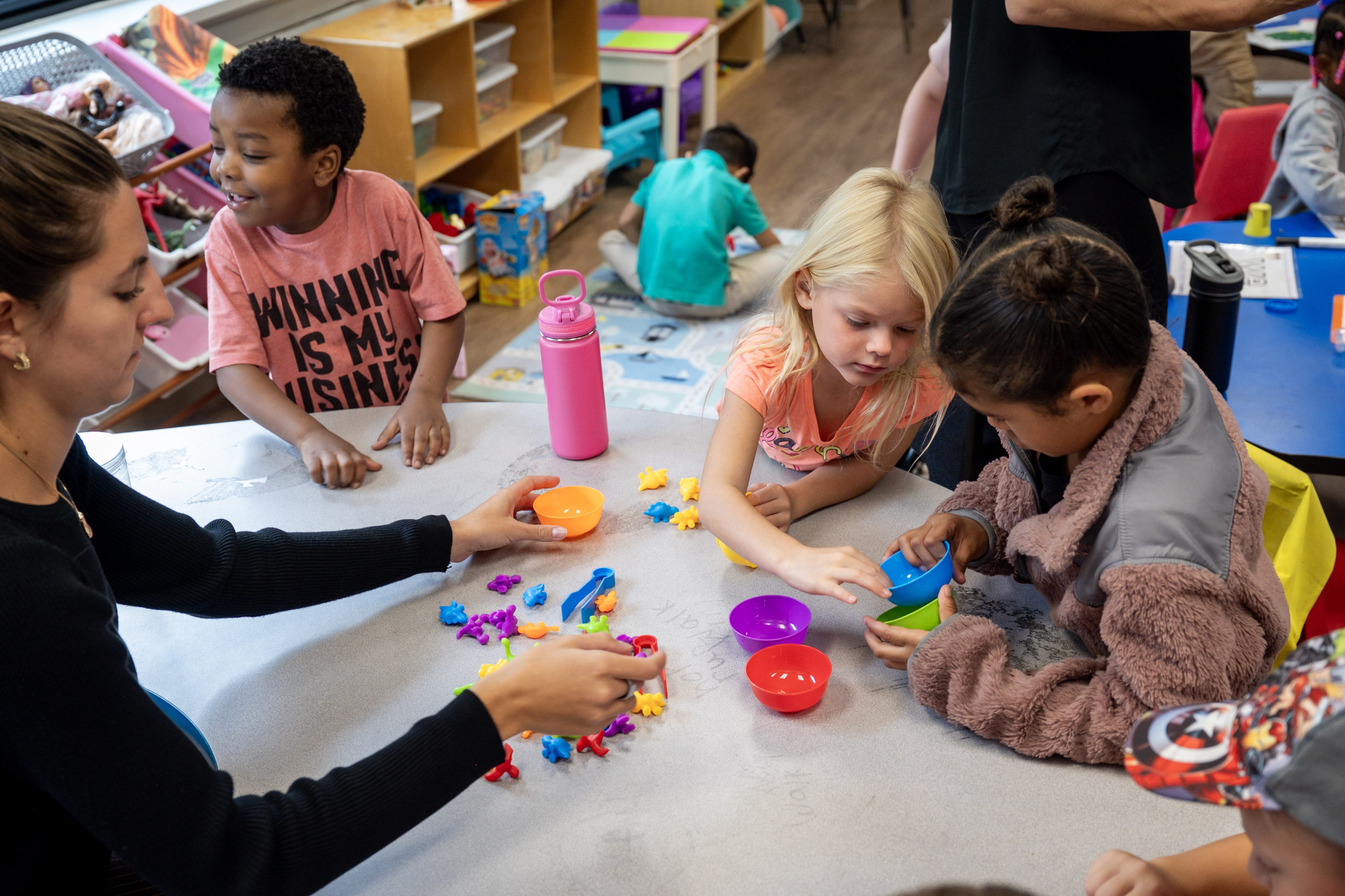Adult and children playing with colorful sorting toys at a table.