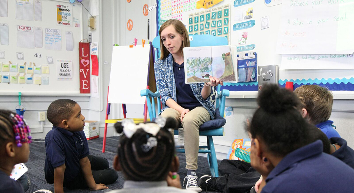 Adult reads illustrated book to children sitting on floor.